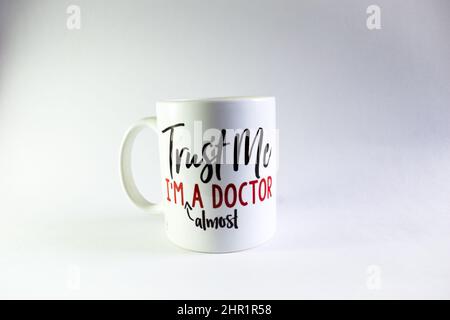 A picture of a white cup with printing " Trust me I'm almost a doctor" in a white background Stock Photo