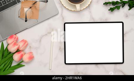 Top view, Feminine office desk workspace in white marble background with digital tablet white screen mockup, tulips flowers, laptop, glasses and decor Stock Photo