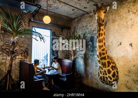 Bangkok, Thailand. 25th Feb, 2022. A couple seen discussing during dessert next to a taxidermy giraffe on the wall at the hotel bar in Bangkok. Daily life around Bangkok as Thailand prepares to relax requirements for the 'Test and Go' program, its quarantine-free entry scheme for fully-vaccinated international tourists. The easing of entry requirements comes as the country is experiencing a surge in COVID-19 infections, averaging over 20,000 reported cases per day. Credit: SOPA Images Limited/Alamy Live News Stock Photo