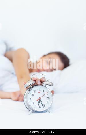 5 more minutes.... Shot of a sleepy young woman reaching out to turn off her alarm clock. Stock Photo