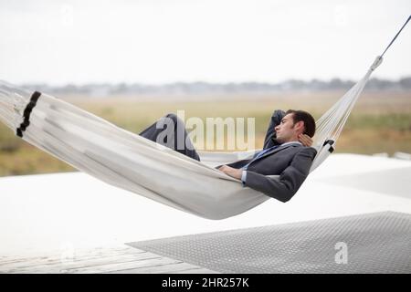 Taking in the landscape. A young executive in a suit taking in the landscape from a hammock. Stock Photo