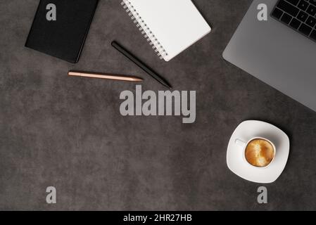 Workspace top view with laptop, notepad, pens and coffee on dark grey stone background. Flat lay with copy space. Business concept. Stock Photo