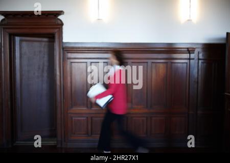 In a hurry with important documents. Side view of a female legal person walking quickly with some documents. Stock Photo