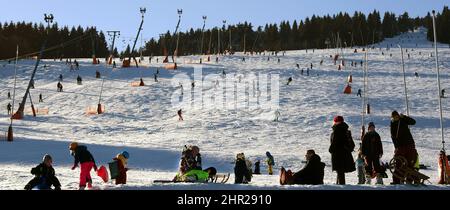 Oberwiesenthal, Germany. 24th Feb, 2022. Tourists stand at the foot of the Fichtelberg, where skiers and skateboarders are on the road. With beautiful weather and partial sunshine, many winter sports enthusiasts and tourists took advantage of the snow-covered slopes. Credit: Waltraud Grubitzsch/dpa-Zentralbild/ZB/dpa/Alamy Live News Stock Photo