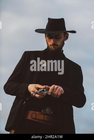 Cowboy shooter in black suit and cowboy hat. Serious man with wild west guns, retro pistol revolver and marshal ammunition. American western Sheriff Stock Photo