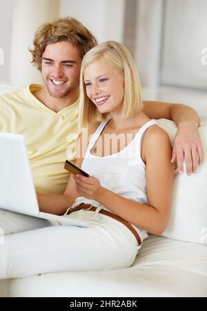 Searching for something for their new house. A happy young couple doing their online banking from the comfort of their couch. Stock Photo