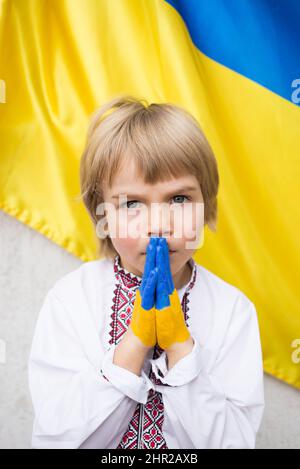 Children's hands are painted in the colors of the Ukrainian flag. A boy in national Ukrainian clothes asks for help. Stop the war in Ukraine. national Stock Photo