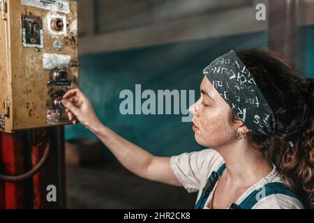The concept of small business, feminism and women's equality. A young tired woman presses a button on the factory working mechanism. Stock Photo