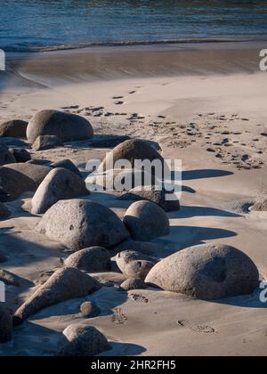 Boulder in the beach with human foot prints going to the water. Stock Photo