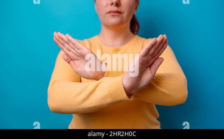 Angry caucasian 20s woman in yellow sweater crossing hands makes stop gesture, demonstrates rejection isolated over blue background. Stock Photo