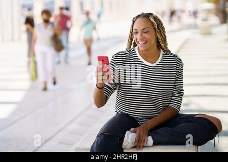Smiling black woman surfing smartphone in city Stock Photo
