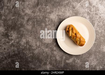 Chocolate Chip Brioche Roll on a white plate against a grey textured concrete background flat lay. Stock Photo