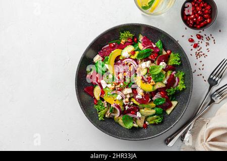 Beetroot salad with avocado, cucumber, feta and pomegranate, seasoned with sesame seeds and flax on a gray background. Top view, copy space. Stock Photo