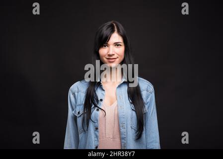 Portrait of attractive and happy caucasian brunette girl in shirt isolated on black studio background. Stock Photo