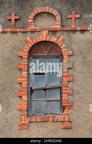 Old, tumbledown christian window surrounding red brick edges. Stock Photo