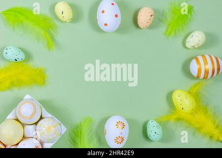 Top view of Easter eggs in an egg stand, painted with different patterns and feathers on a green background. Place for text. Easter concept. Stock Photo
