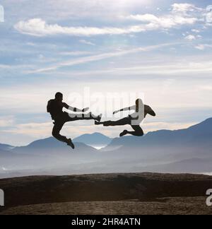 Flying feet on a mountain. Two male kickboxers fly kicking one another on a mountain top. Stock Photo