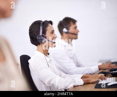 Happy to be helpful. Shot of two help desk operators wearing headsets and working at their computers. Stock Photo