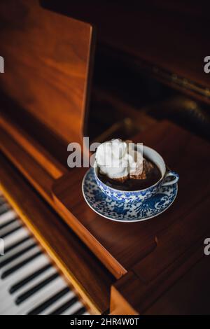 Hot drinking chocolate in blue floral teacup set with white meringue sitting on baby grand piano Stock Photo