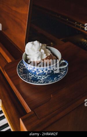 Hot drinking chocolate in blue floral teacup set with white meringue sitting on baby grand piano Stock Photo