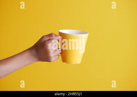 close up of man hand holding mug isolated on yellow  Stock Photo
