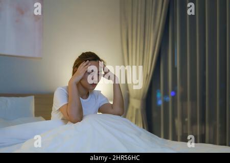 Asian woman lying on a white bed in the bedroom looking worried or thinking about something about her life or work in mid night at home. Stock Photo