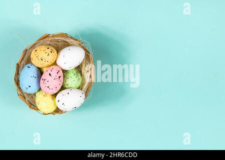 Multi-colored Easter eggs in a nest on a blue background with space for text, lettering. Basis for a postcard, Top view. Stock Photo