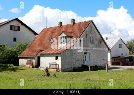 Abandoned small old suburban family house with dilapidated damaged white facade and red roof tiles mixed with rusted metal tiles covering broken roof Stock Photo