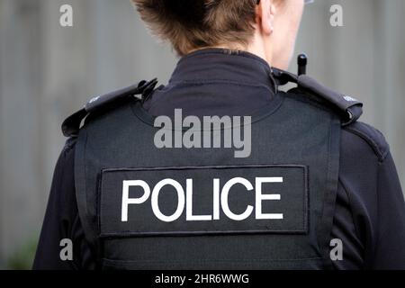 A rear view of a British female police officer in full uniform and wearing body armour. The image clearly shows the officers police insignia Stock Photo