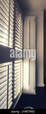Vertical image of light shining through window with plantation shutters Stock Photo