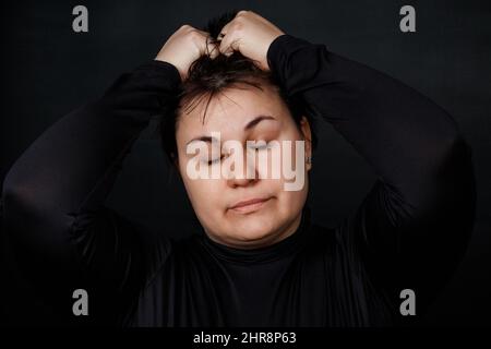 brunette woman holding on to her head closing her eyes on a black background. High quality photo Stock Photo