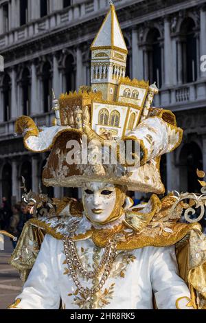 Venice, Italy. 25th Feb, 2022. Colourful costumes at the Carnival in Venice 2022. Man in costume wearing a large hat with Venetian landmarks in St. Mark's Square. Credit: Vibrant Pictures/Alamy Live News Stock Photo