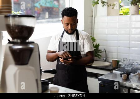 Young male african american barista using tablet pc while working in coffee shop Stock Photo