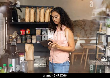 Young african american female barista using digital tablet while working at coffee shop Stock Photo