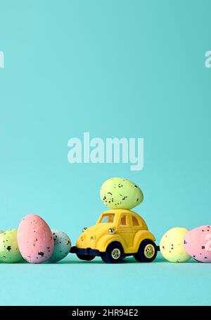 One Easter egg on a small car on a blue background with colorful eggs. Copy space. Easter card. Stock Photo