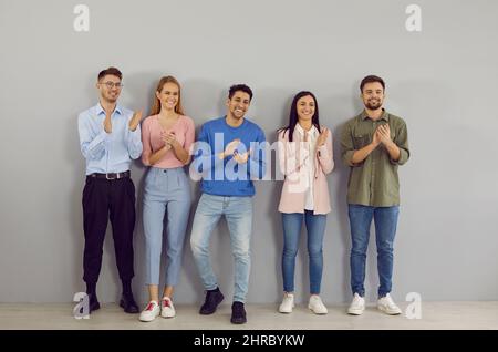 Friendly and happy young successful people stand in line and applaud their leader. Stock Photo