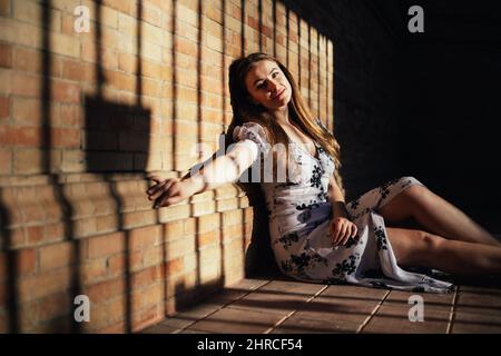 Caucasian woman sitting on floor leaning against brick wall and smiling at camera Stock Photo