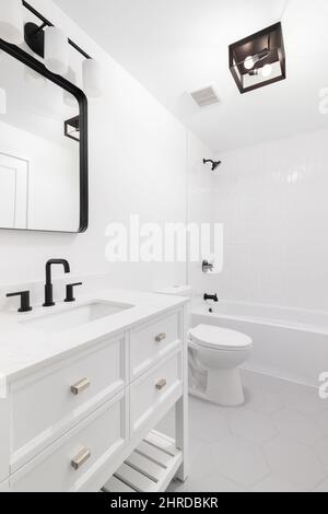 A white bathroom with a grey hexagon tile floor, black lights and faucet, and a white tiled shower. Stock Photo