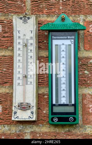 Analogue and digital maximum minimum thermometers hanging on a wall in a garden. Stock Photo