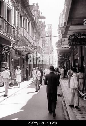 1940s NARROW STREET RUA OUVIDOR A BUSY SHOPPING STREET WITH LOTS OF SMALL SHOPS AND PEDESTRIANS IN RIO DE JANEIRO BRAZIL - r12253 PAL001 HARS SOUTH AMERICA SHOPPERS SOUTH AMERICAN ADVENTURE AND OPPORTUNITY NARROW STORES RIO LOTS DE CITIES STYLISH BRAZILIAN COMMERCE COOPERATION JANEIRO RIO DE JANEIRO SOUTHERN HEMISPHERE BLACK AND WHITE BUSINESSES HISPANIC ETHNICITY OLD FASHIONED Stock Photo