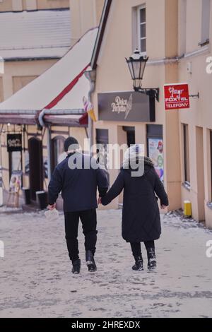 Elderly couple hold hands while walking on a street with cafes in the city center Stock Photo