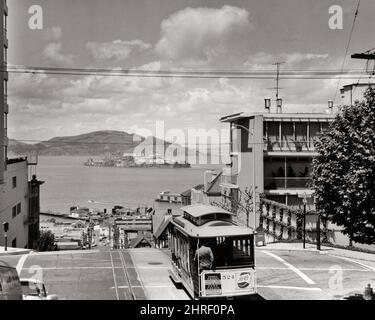 1960s PUBLIC TRANSPORTATION CABLE CAR ABOUT TO DESCEND HILL WITH VIEW TO ALCATRAZ ISLAND AND PRISON IN BAY SAN FRANCISCO CA USA - r952 FST001 HARS FRANCISCO SADNESS NORTH AMERICA NORTH AMERICAN HIGH ANGLE DIRECTION IN THE TO CA TROLLEY WEST COAST CONCEPTUAL DESCEND CITIES ESCAPE CABLE CAR PANORAMIC SAN FRANCISCO BLACK AND WHITE CABLE ICONIC OLD FASHIONED Stock Photo