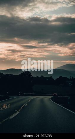 Vertical of an asphalt road against mountains covered with forests at sunset in Konigssee, Bavaria Stock Photo