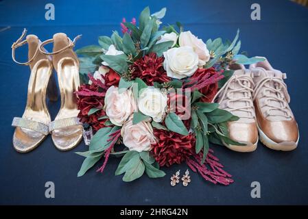 Closeup shot of the female and male wedding rose gold shoes, earrings and a bouquet Stock Photo