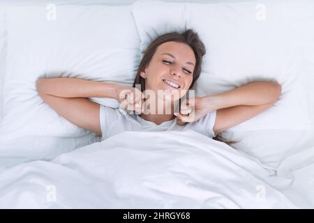 Good morning. Attractive woman wakening up happy. Top view of beautiful woman lying on comfortable white bed and stretching hands Stock Photo