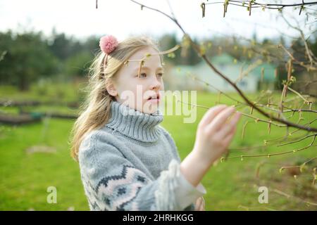 Cute young girl admiring fresh new soft buds sitting on chestnut tree branches. Early spring in a city. Stock Photo