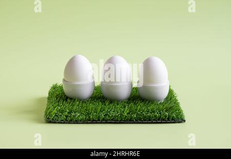 Easter eggs. Three chicken eggs in stands on a green background. Healthy organic food concept. Copy space. Stock Photo