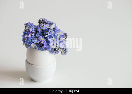 Bouquet of blue forget-me-not flowers in a cracked egg on a white background. Easter minimal concept. Copy space. Stock Photo