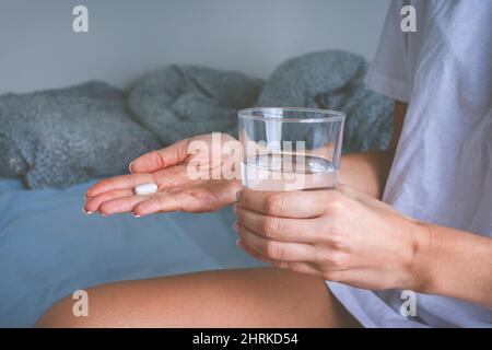 Woman holding glass of still water and taking painkiller from headache pain. Woman taking pills or antidepressant Stock Photo