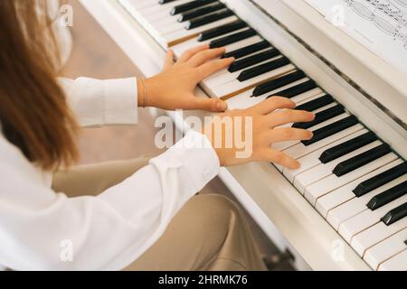 Close-up top view of unrecognizable musician female pianist playing gentle music on white classical piano in light classroom. Stock Photo